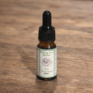 Amber glass dropper bottle of Rose flower essence with printed botanical label, photographed on a rustic wooden surface in natural light.